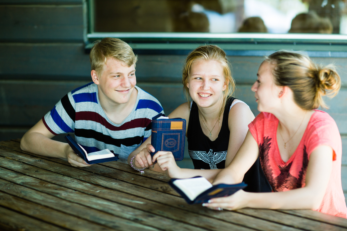 Kolme nuorta pöydän ääressä Raamattu kädessään.