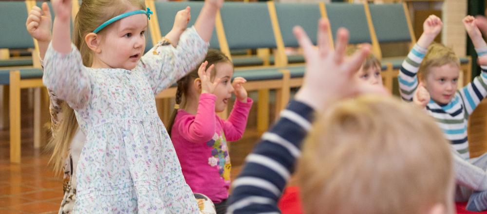 Lapsia laulamassa ja leikkimässä kädet ylhäällä.