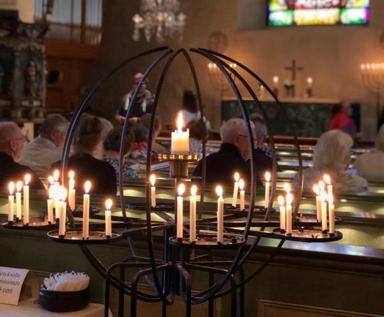 Pohjan kirkon lähetyskynttelikkö, jossa palavia kynttilöitä ja penkeissä ihmisiä istumassa.