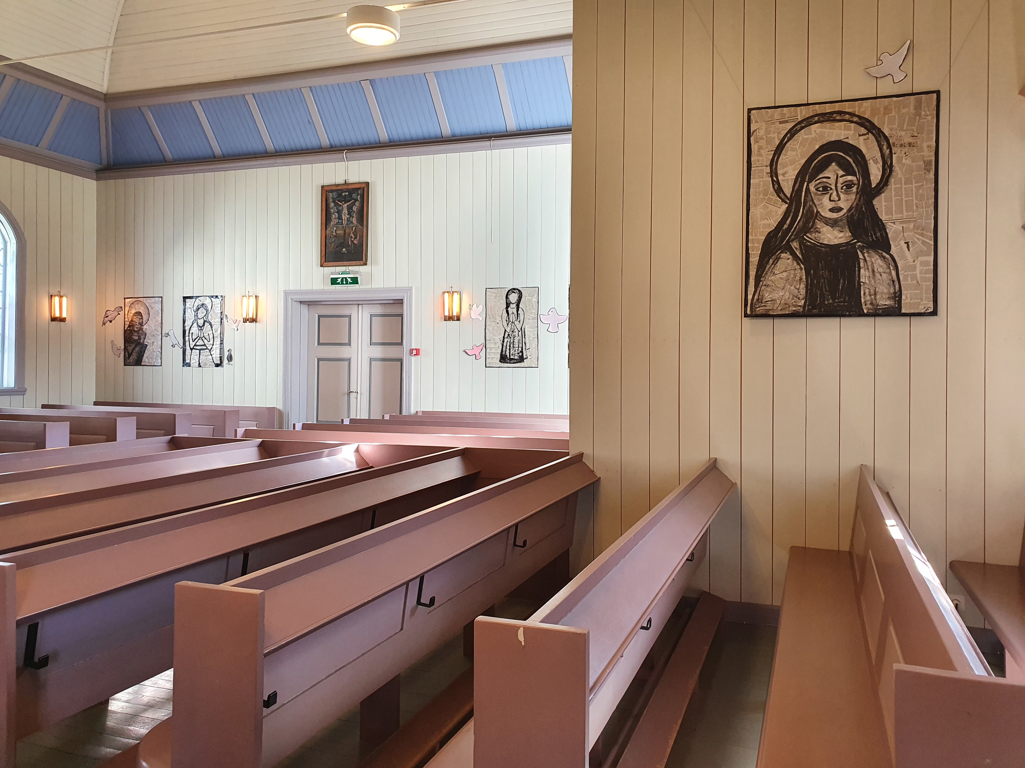 Mustion kirkkosali, jossa puisia penkkirivejä. Seinillä oppilastöitä Neitsyt Mariasta. Tauluissa pohjakankaana käytetty sanomalehtipaperia ja maalaamiseen mustaa maalia.